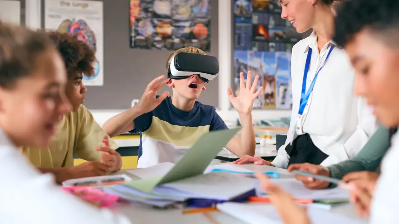 Chłopiec w goglach VR przeżywa lekcję, a nauczycielka z uśmiechem obserwuje tę innowację pedagogiczną.