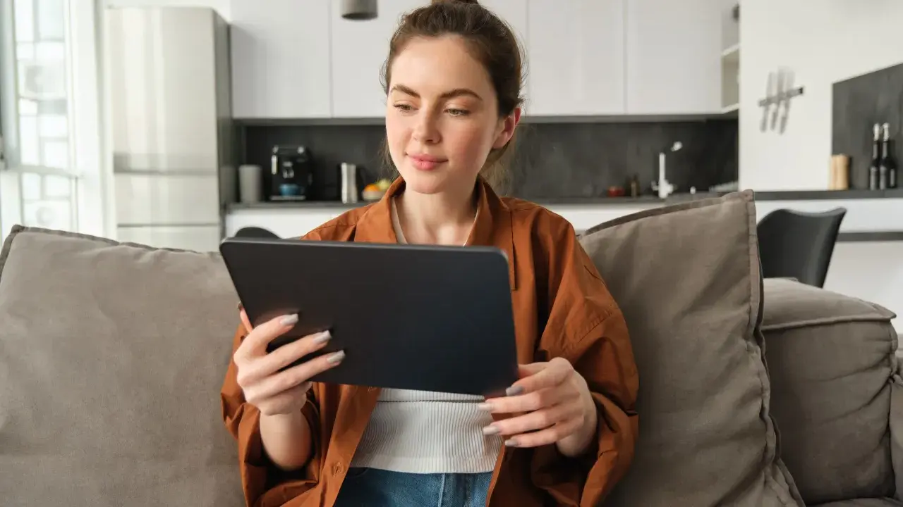 Kobieta na kanapie przegląda tablet, być może szukając informacji o kursach fakultatywnych.