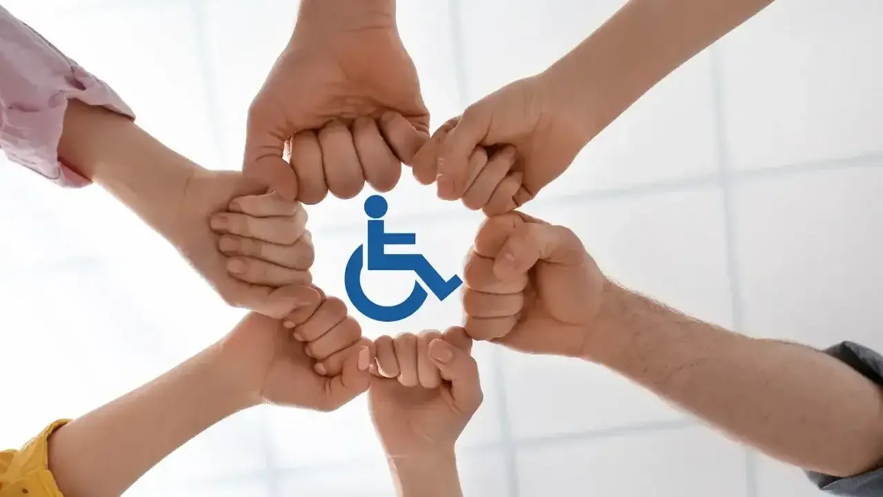 Dłonie tworzą krąg wokół symbolu niepełnosprawności, symbolizując wsparcie i integrację.