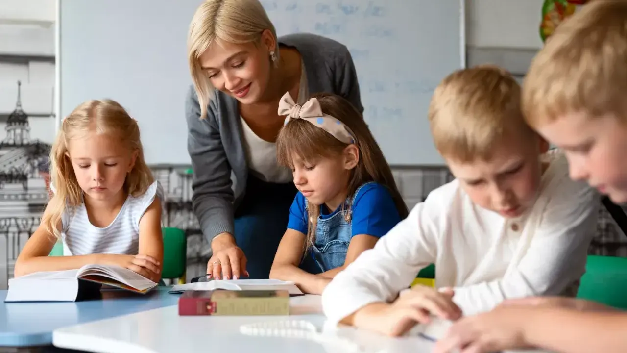 Nauczycielka, jak dobry oligofrenopedagog, wspiera dzieci w nauce przy stolikach.