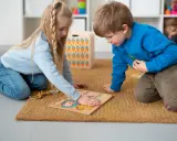 Dzieci na dywanie układają puzzle, ćwicząc spostrzegawczość. To nauka przez zabawę, zgodna z metodą Montessori.