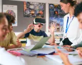 Chłopiec w goglach VR przeżywa lekcję, a nauczycielka z uśmiechem obserwuje tę innowację pedagogiczną.