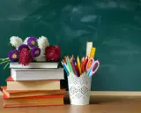 Kwiaty na stosie książek i przybory szkolne na tle zielonej tablicy. Idealna kompozycja na Dzień Edukacji Narodowej.