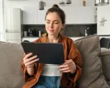 Kobieta na kanapie przegląda tablet, być może szukając informacji o kursach fakultatywnych.