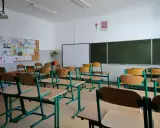 Pusta klasa szkolna z rzędami ławek i krzeseł. Na ścianie tablica, projektor i dziecięce rysunki. Wygląda na to, że **odwołane zajęcia w szkołach** sprawiły, że nikt dziś nie przyszedł.