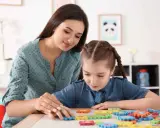 Kobieta pomaga dziewczynce z niepełnosprawnością intelektualną w stopniu lekkim układać kolorowe puzzle.