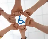 Dłonie tworzą krąg wokół symbolu niepełnosprawności, symbolizując wsparcie i integrację.