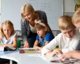 Nauczycielka, jak dobry oligofrenopedagog, wspiera dzieci w nauce przy stolikach.