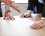 Dłonie nad dokumentem na biurku. Dyskusja nad treścią, być może art. 30 kp.