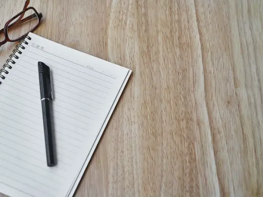 Notatnik, długopis i okulary na drewnianym blacie. Czas na spisanie opinii o uczniu.