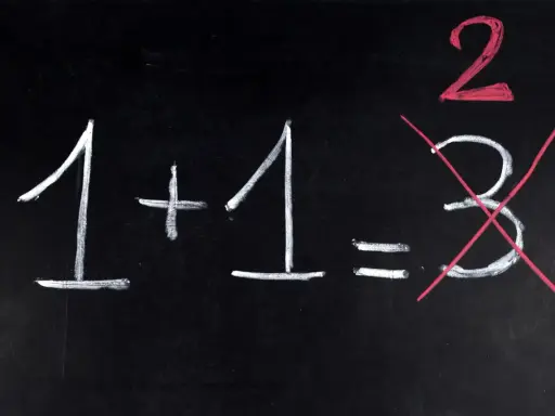 Na czarnej tablicy napisano kredą: 1+1=2. Liczba 3 jest przekreślona, jakby to był trudny egzamin dojrzałości.