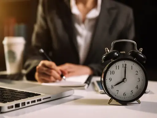 Zegar pokazuje 8:00. Zastanawiasz się, ile to godzin przy pracy na 1/2 etatu? Obok laptop, notatnik i kawa.