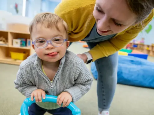 Chłopiec z zespołem Downa, w okularach, z językiem na brodzie, bawi się z terapeutką. To przykład pracy w obszarze oligofrenopedagogiki.
