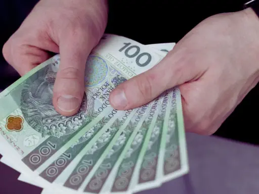 Dłonie trzymają stos banknotów 100 zł. Czy to wypłata z UoP?