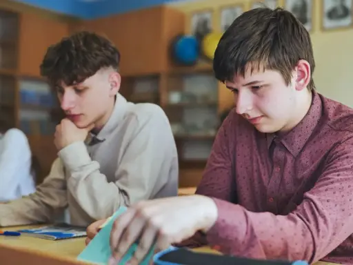 Uczniowie w klasie, jeden z nich zamyślony, inny przegląda notatki. Czyżby czekał na ocenę, która może oznaczać nieklasyfikowanie ucznia?