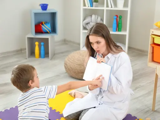Terapeuta pracuje z dzieckiem, pomagając mu w terapii afazji. Pokazuje mu książkę, ćwicząc mowę i komunikację.