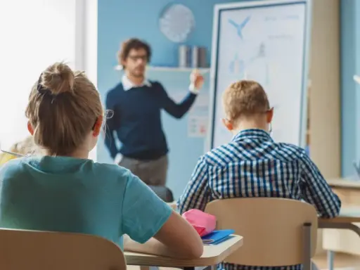 Nauczyciel mianowany zarobki - młody mężczyzna tłumaczy coś uczniom przy tablicy w jasnej sali lekcyjnej.