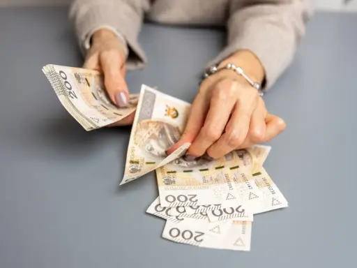 Dłonie liczą banknoty 200 zł. To może być wypłata świadczenia urlopowego na wymarzone wakacje.