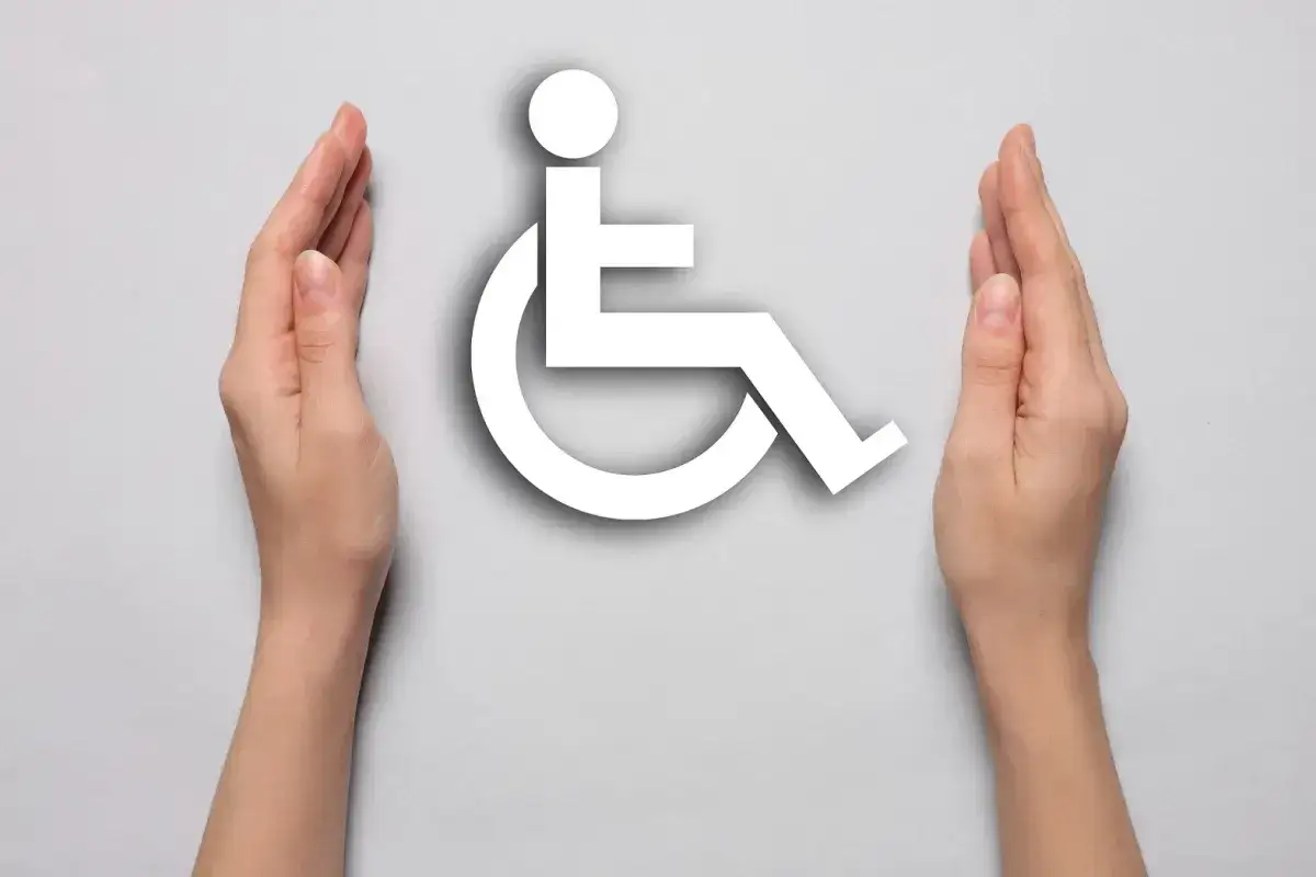 Dłonie otaczają białe symbole niepełnosprawności, symbolizując wsparcie i akceptację.