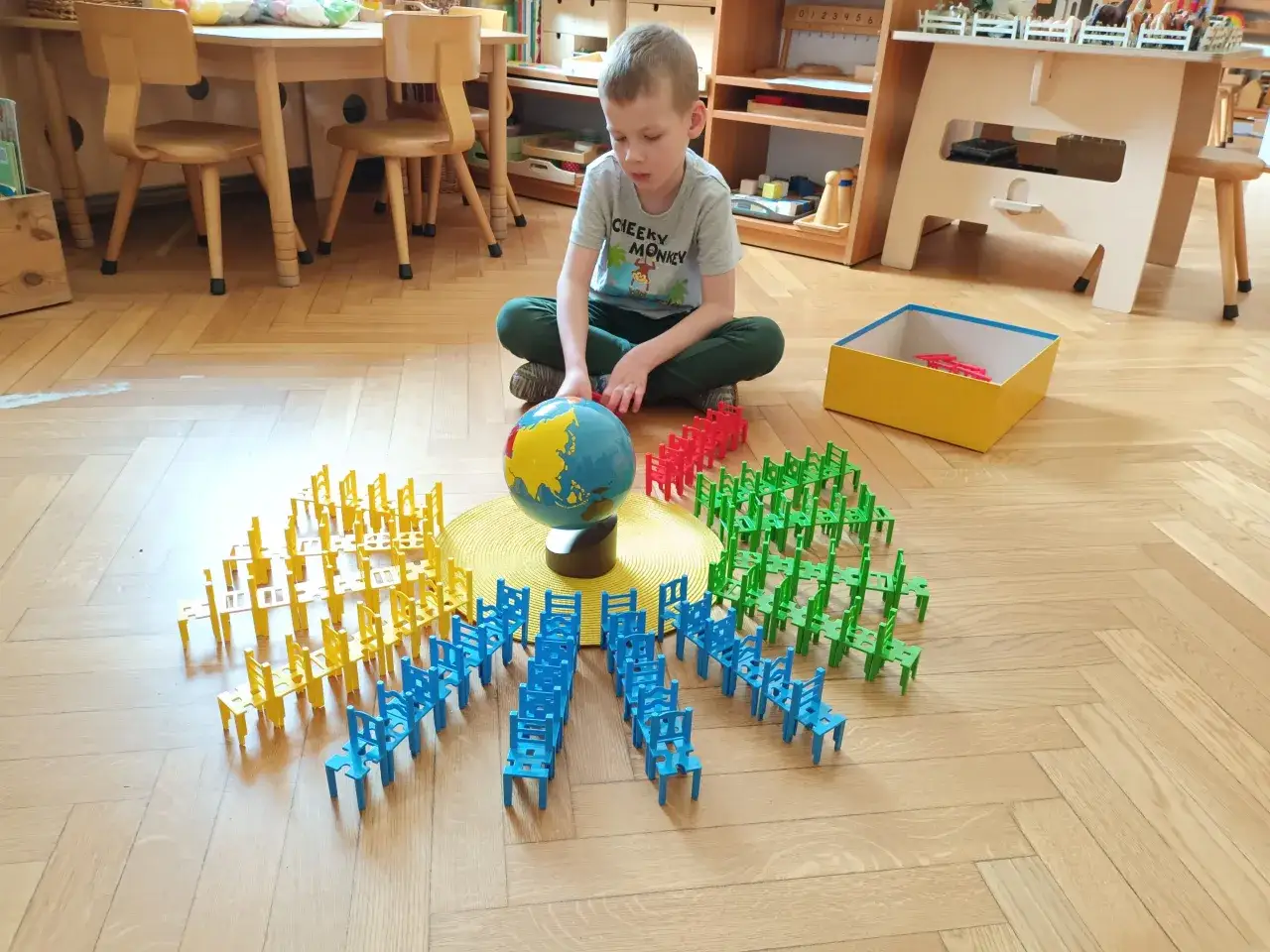 Chłopiec bawi się klockami w kształcie krzesełek, tworząc z nich okręgi wokół globusa. To świetna zabawa edukacyjna w stylu metoda montessori.