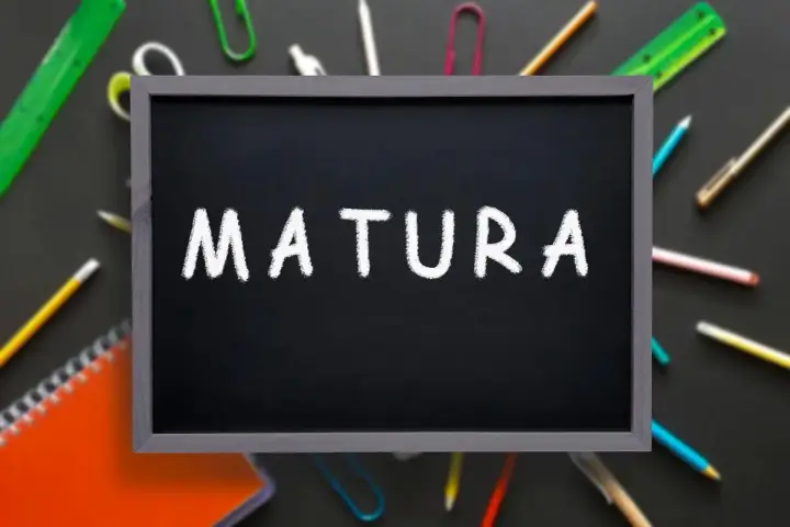 Czarna tablica z napisem "MATURA" kredą, otoczona przyborami szkolnymi. To symbol ważnego świadectwa dojrzałości.