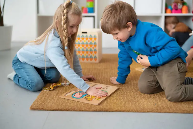 Dzieci na dywanie układają puzzle, ćwicząc spostrzegawczość. To nauka przez zabawę, zgodna z metodą Montessori.