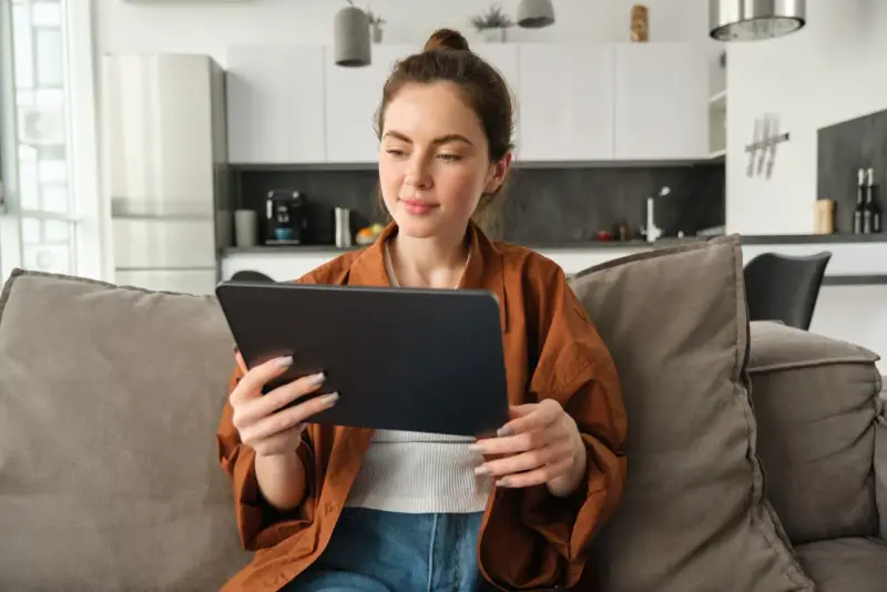 Kobieta na kanapie przegląda tablet, być może szukając informacji o kursach fakultatywnych.